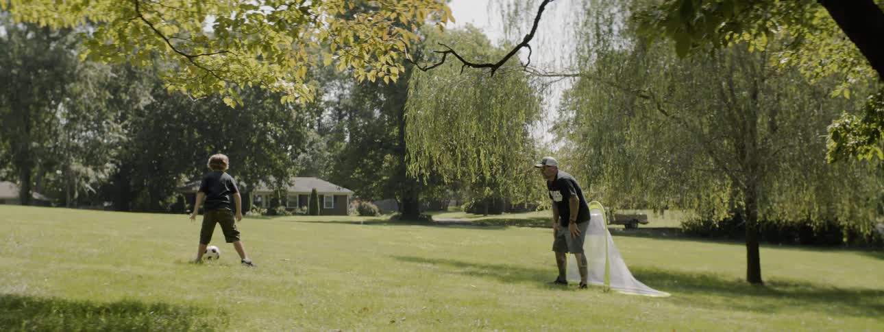 Man and child play with soccer ball in field