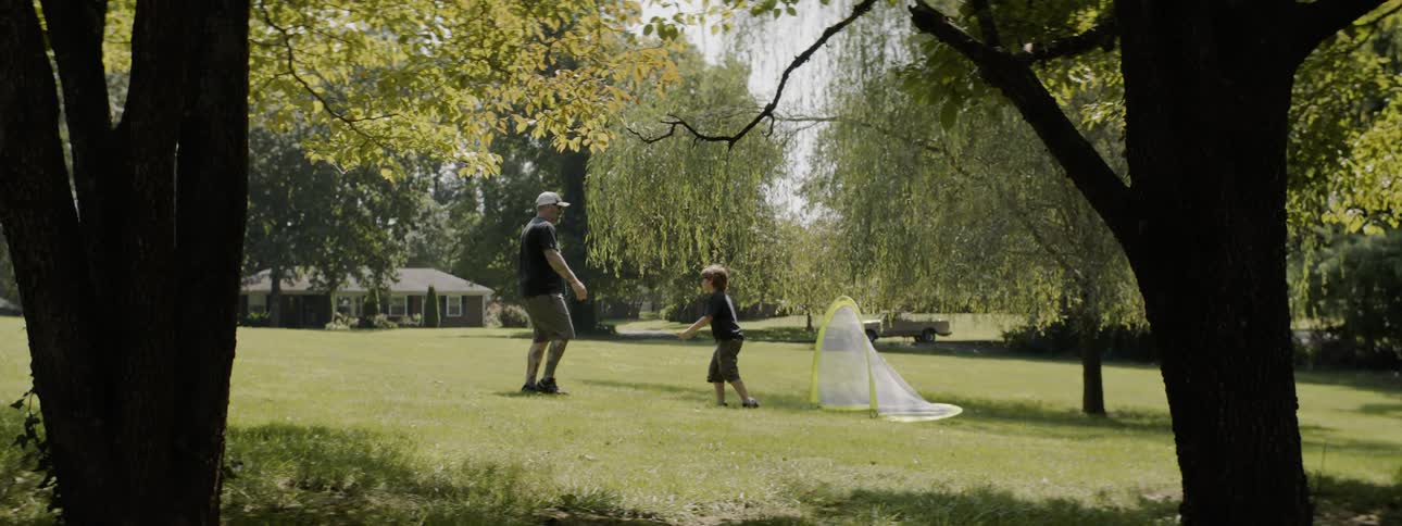 Man and boy play football on the field of grass in the public park during daylight