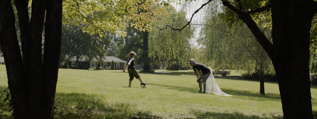 Father and son play soccer on the lawn outside a house