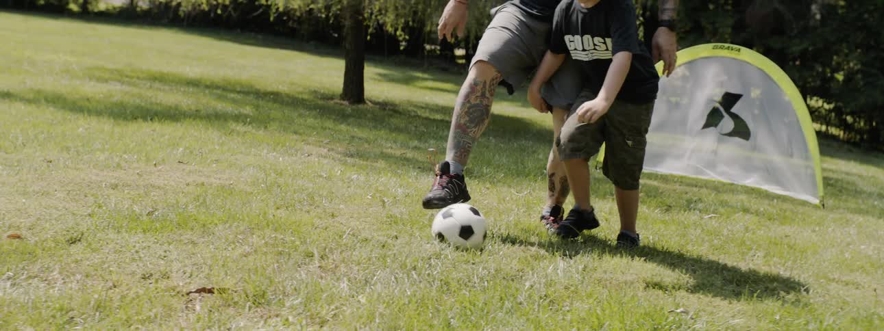 A father and son play soccer in a backyard