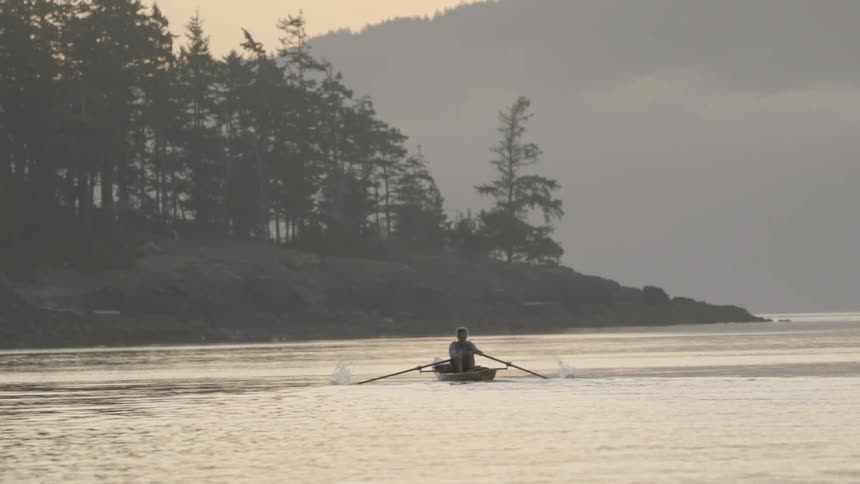 A person rows a boat across a lake