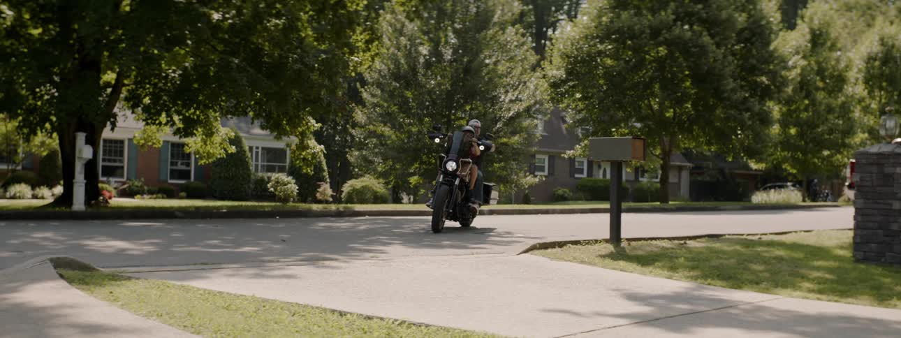 A man driving his son on a motorcycle onto a driveway