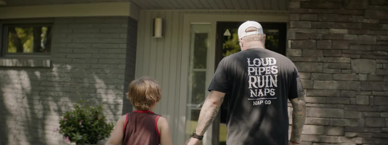 A man and boy holding hands walk towards a house