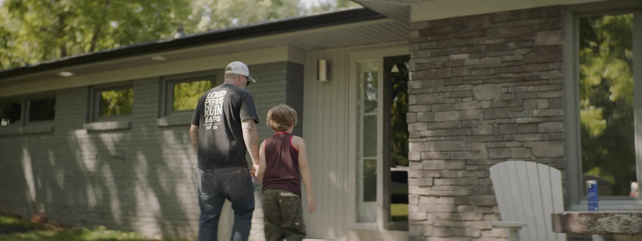 Man and child walks towards home holding hands in the countryside