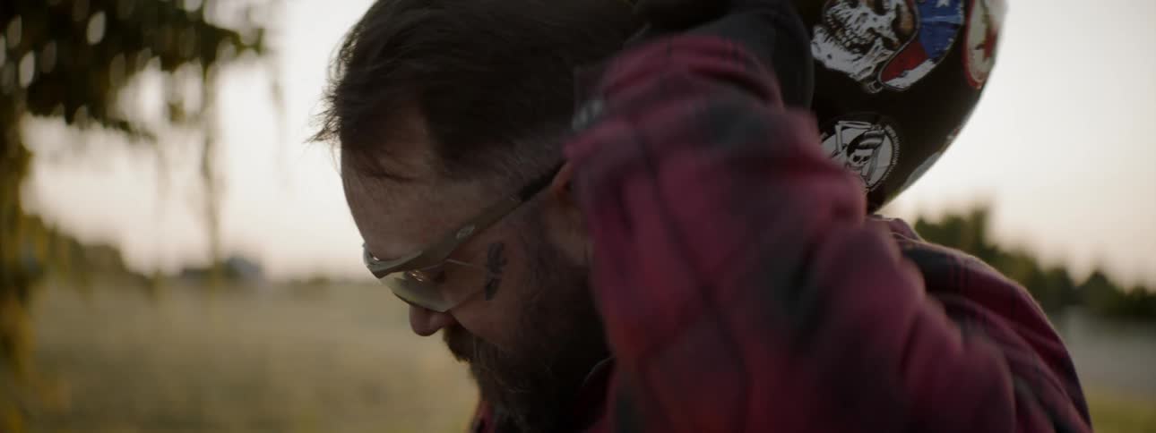 Bearded man wearing goggles takes off his helmet outdoors at sunset