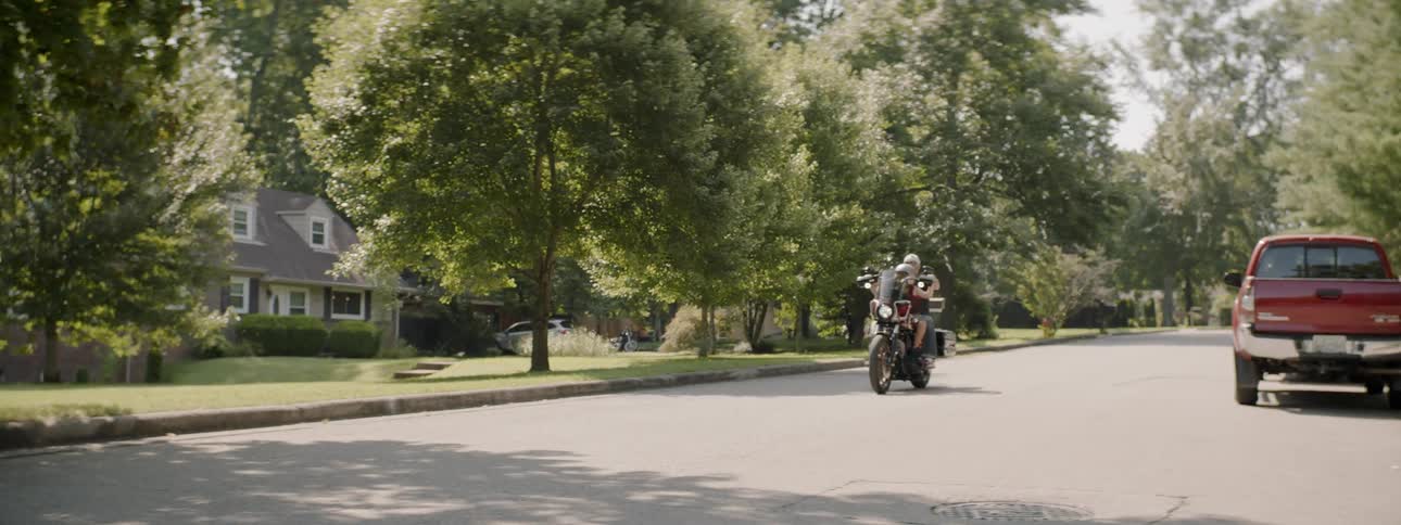 Two people are driving on a motorcycle in a suburban neighborhood