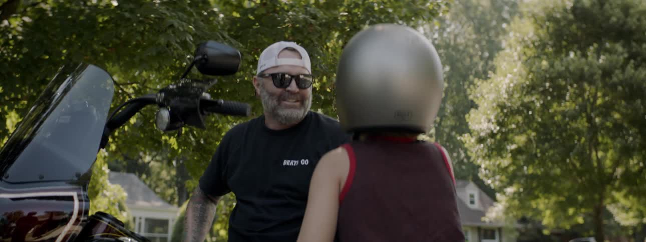 A man sits on a motorcycle and talk to a child wearing a helmet