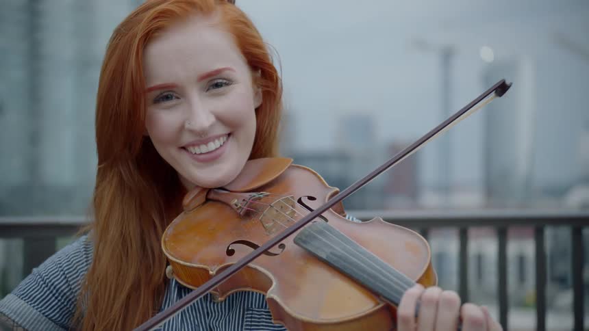 A redhead bows a violin and smiles