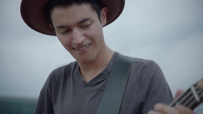 A man in a hat plays a bass guitar and smiles