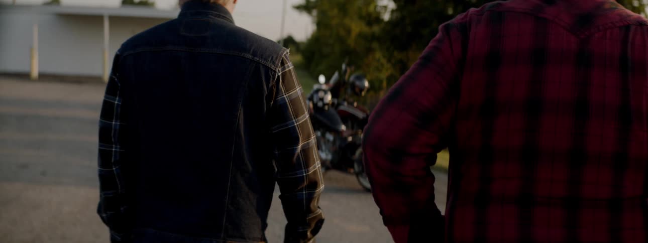 Two males walking on a driveway towards two motorcycles
