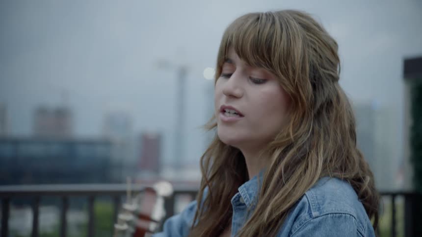 A young woman strumming an acoustic guitar and singing