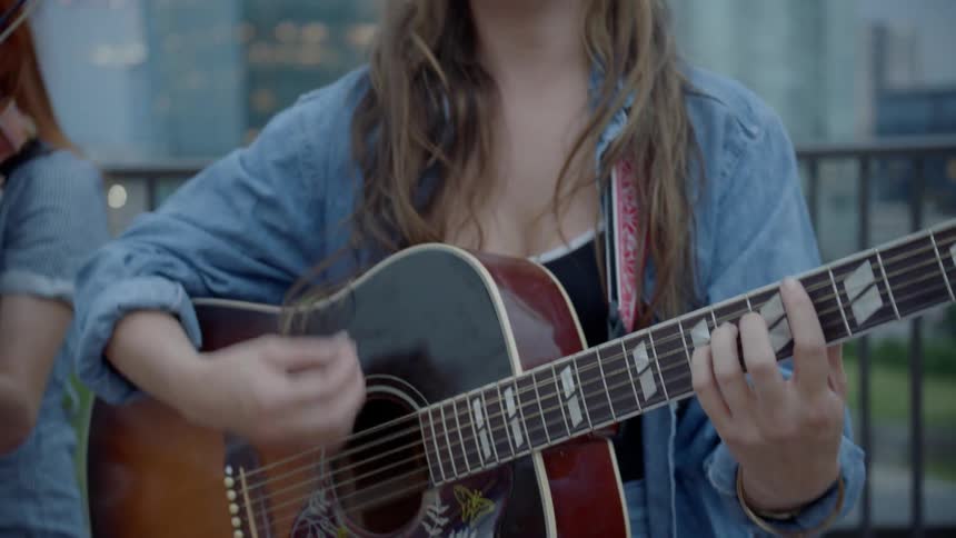 A woman strums a gibson acoustic guitar accompanied by a violinist
