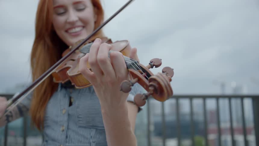 A redheaded woman bows a violin and smiles