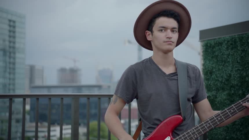 A hat wearing man plays the bass guitar and smiles