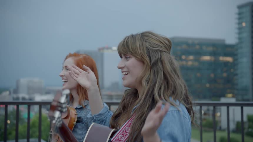 A woman strums a gibson acoustic guitar accompanied by a violinist and takes an applause