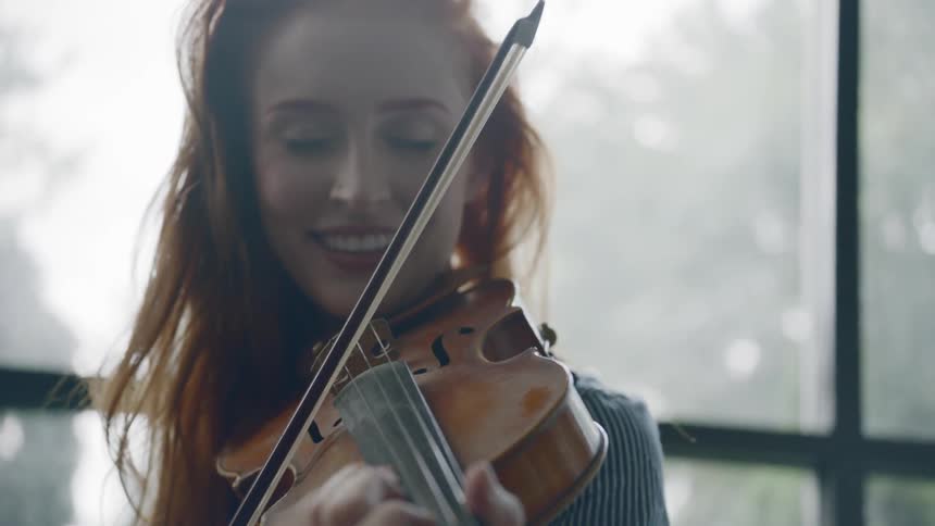 A redheaded woman bows a violin and smiles