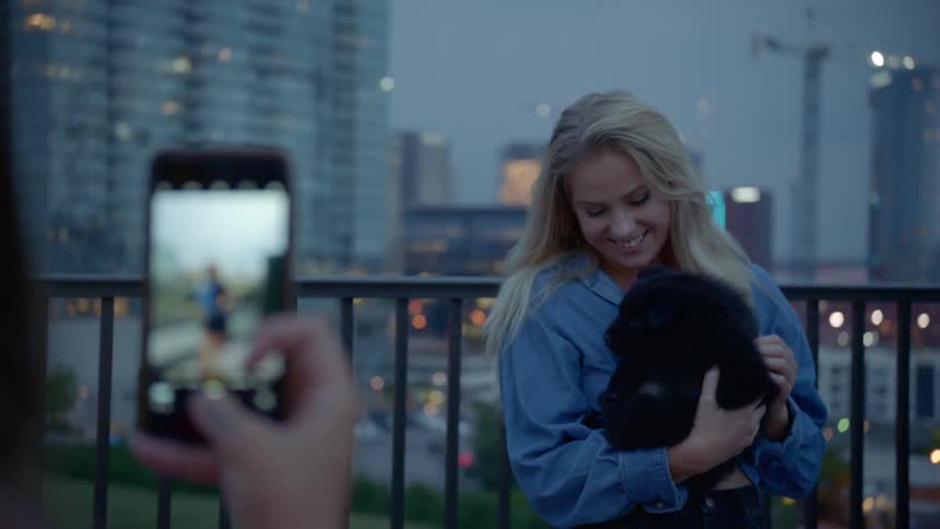 A woman takes a picture of another woman holding a puppy