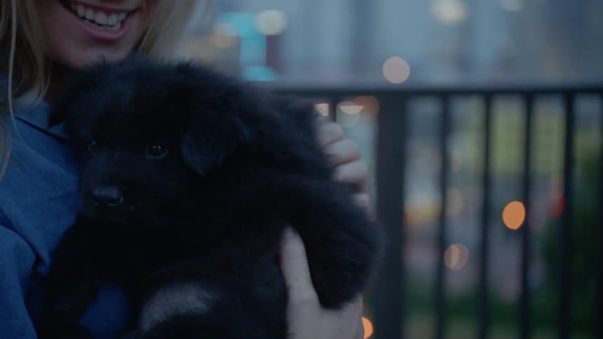 A caucasian female holding and petting a black puppy outside
