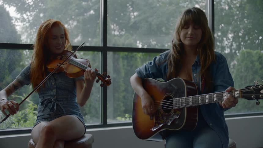 Two young white women play an acoustic guitar and a fiddle