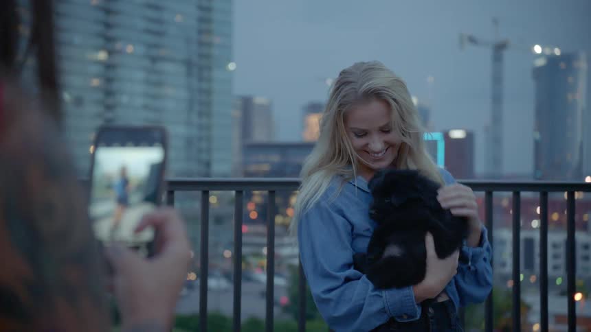 A woman pets a puppy while a friend takes a picture of her