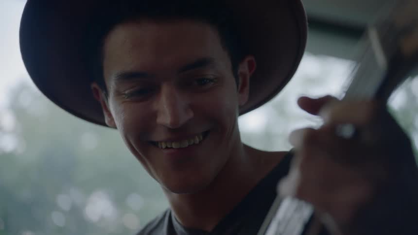 A hat wearing man plays the bass guitar and smiles
