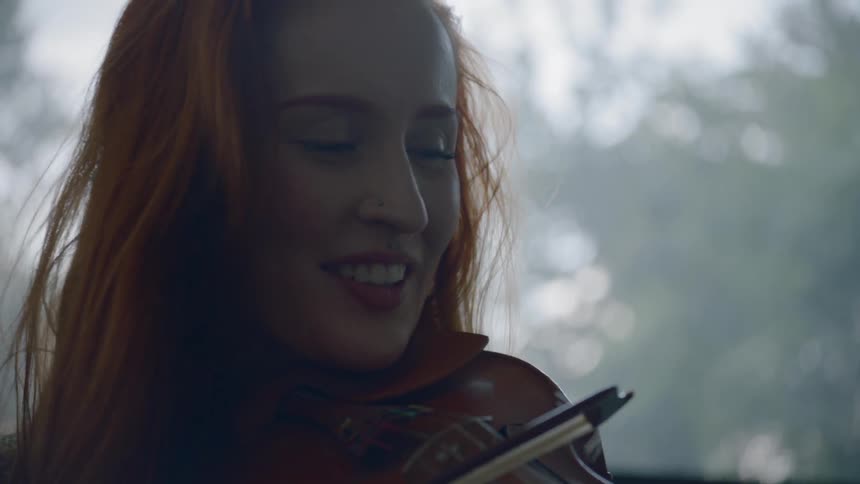 Long ginger hair women play on the violin and smiles during daylight