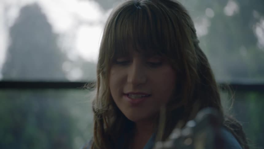 A young woman plays the guitar and sings