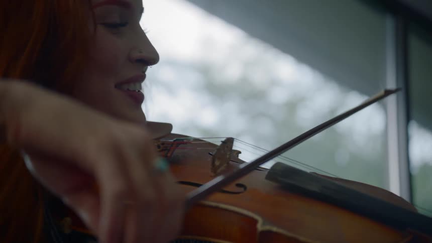 A redheaded woman bows a violin and smiles