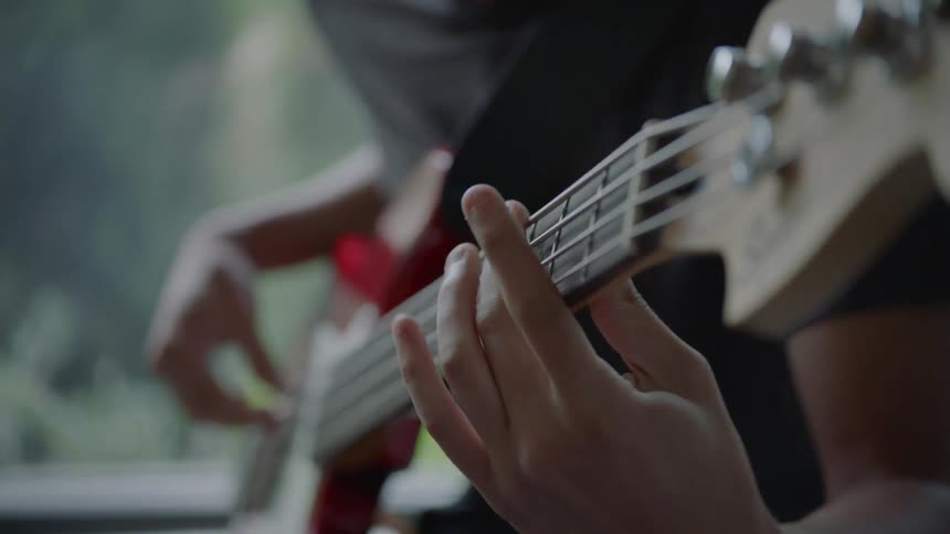 A man playing a guitar sitting by a window