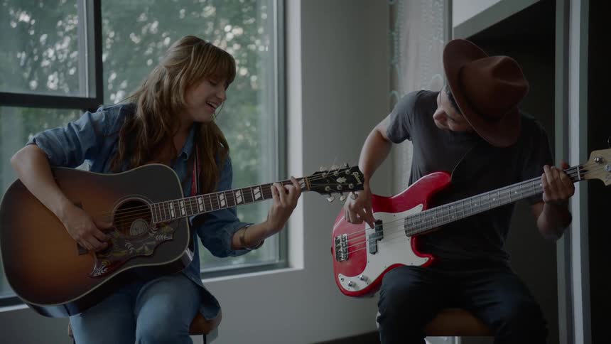 A woman plays guitar while a man in a hat plays bass