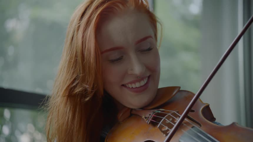A redheaded woman bows a violin and smiles