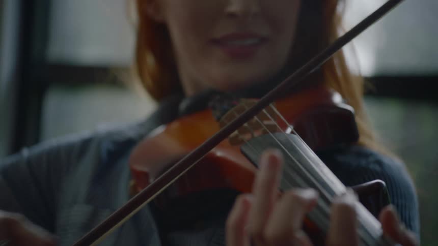 A redheaded woman bows a violin and smiles