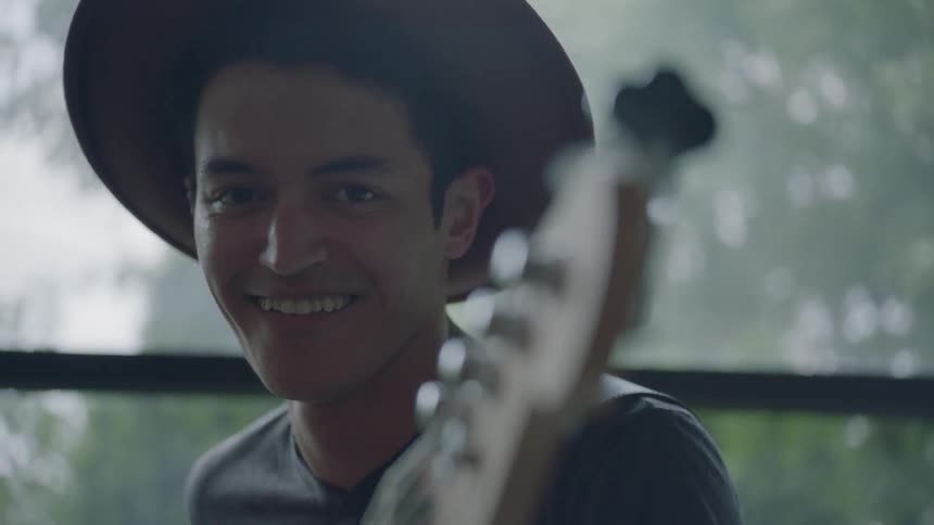 A man is playing guitar indoors while wearing a hat