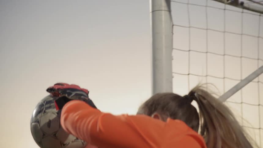 Female soccer goalie catching soccer ball in front of net