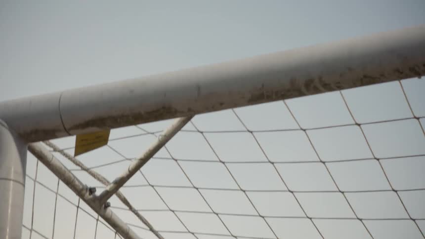 A female goalie jumps to block a soccer ball from the net and catches it