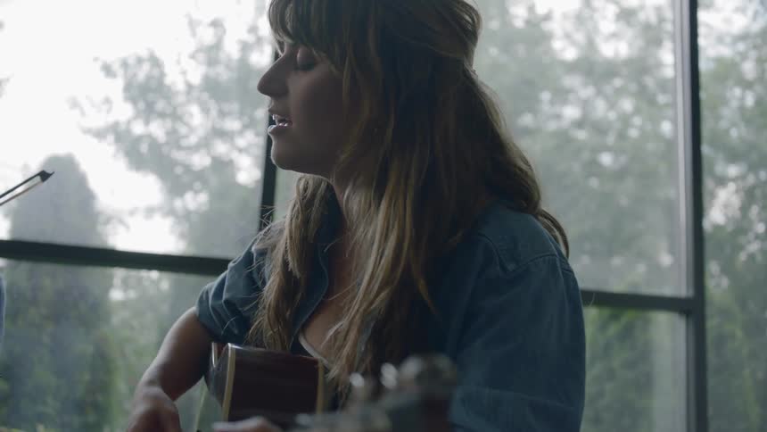 A young woman plays the guitar and sings