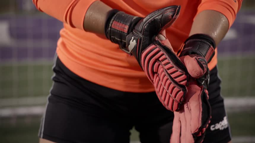 A goalie wears his gloves as he rubs his hand in front of the goal