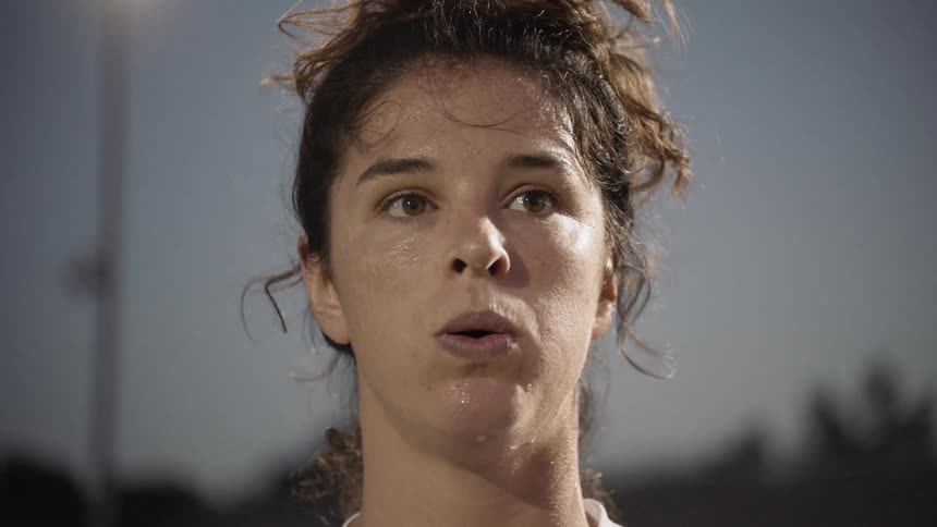 Sweaty football player wearing white football uniform breathes out at dusk