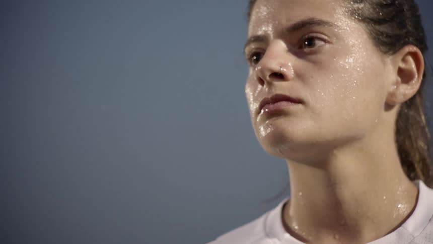 A young girl stands with sweat dripping down her face