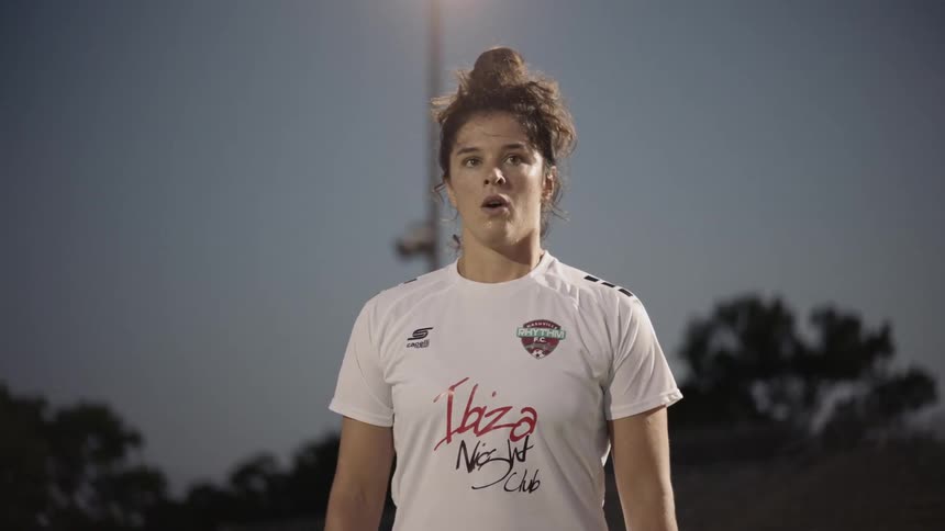 Woman football player wearing white football uniform breathes out at dusk