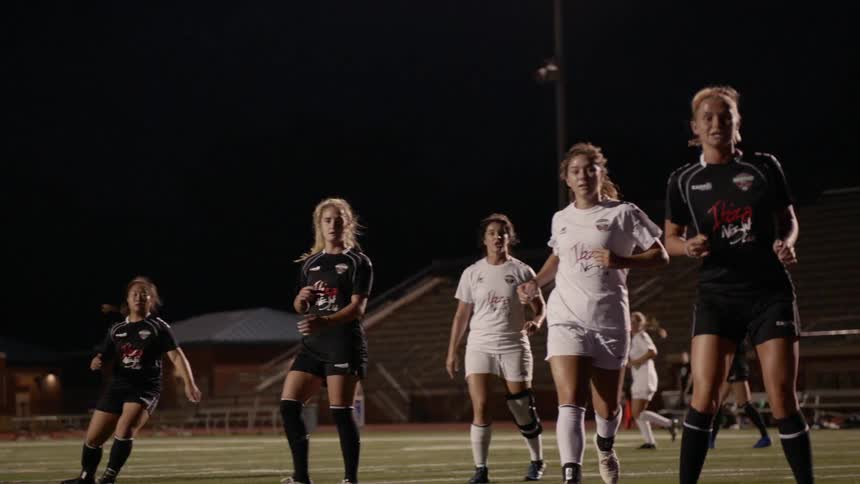 A woman in a white jersey takes a shot in a soccer match