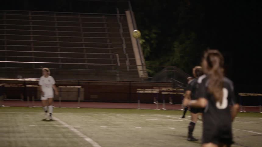 Two teams of women playing soccer at night in a stadium