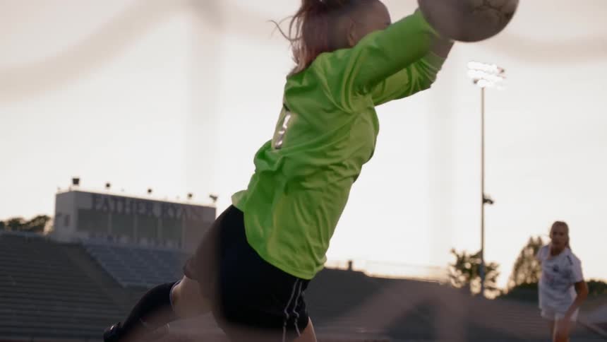 A female goalkeeper attempts to save a shot
