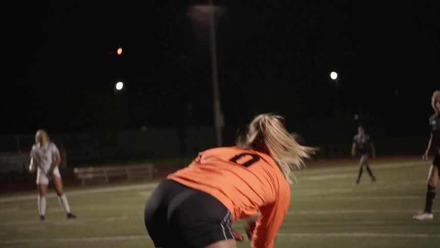A goalkeeper walks with the ball in her hands before rolling it out to her defender in a soccer match