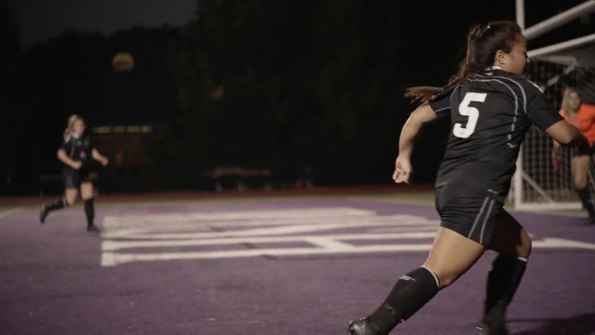 A women's soccer match in which the number nine of a team with a white jersey crosses the ball