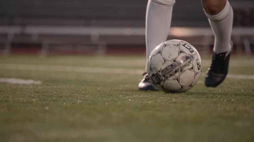 Woman football player plays football in the football field under the stadium lights at night