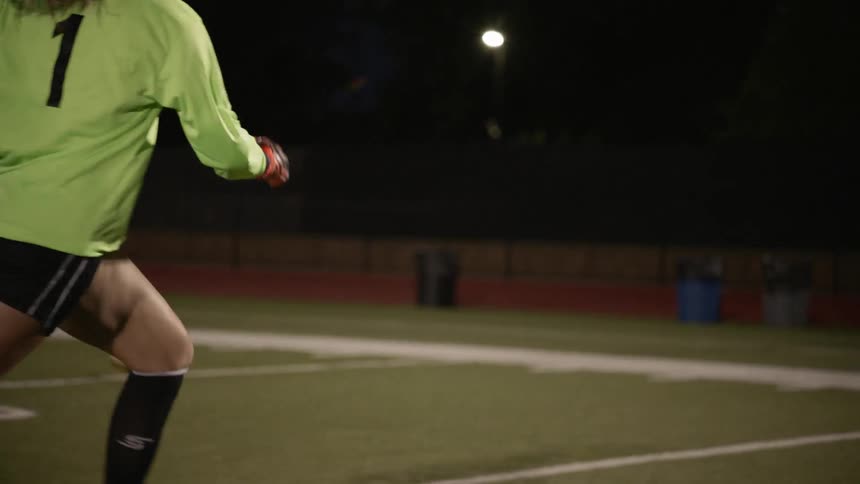 Woman goalkeeper runs towards the ball in the football field at night