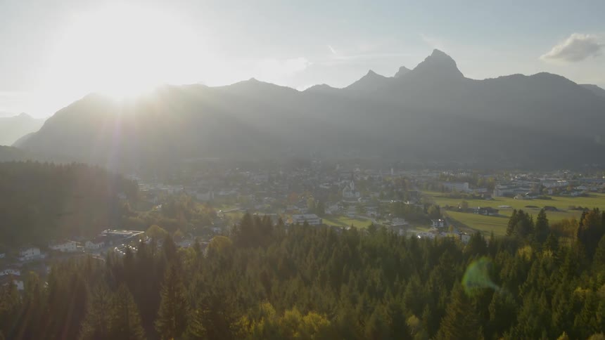 The camera flies over a town nestled below a mountain
