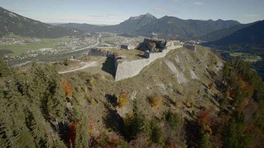 A castle sits on top of a cliff near mountains