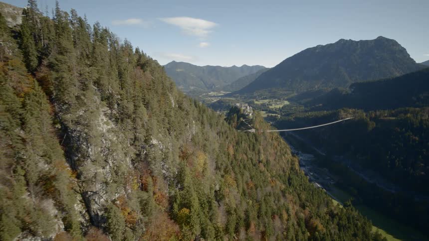 A bridge spans over a river between forests cliffs and hills